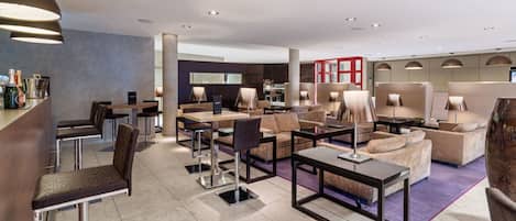 Eine moderne Hotelhalle mit Barbereich, Sitzgelegenheiten und einem sichtbaren Empfangsbereich.