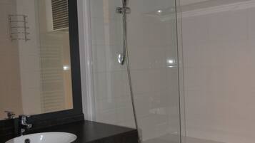 A bathroom with a glass shower enclosure, a white sink, and a dark countertop.