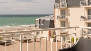 A balcony with a table, a chair, and a view of the beach and ocean.