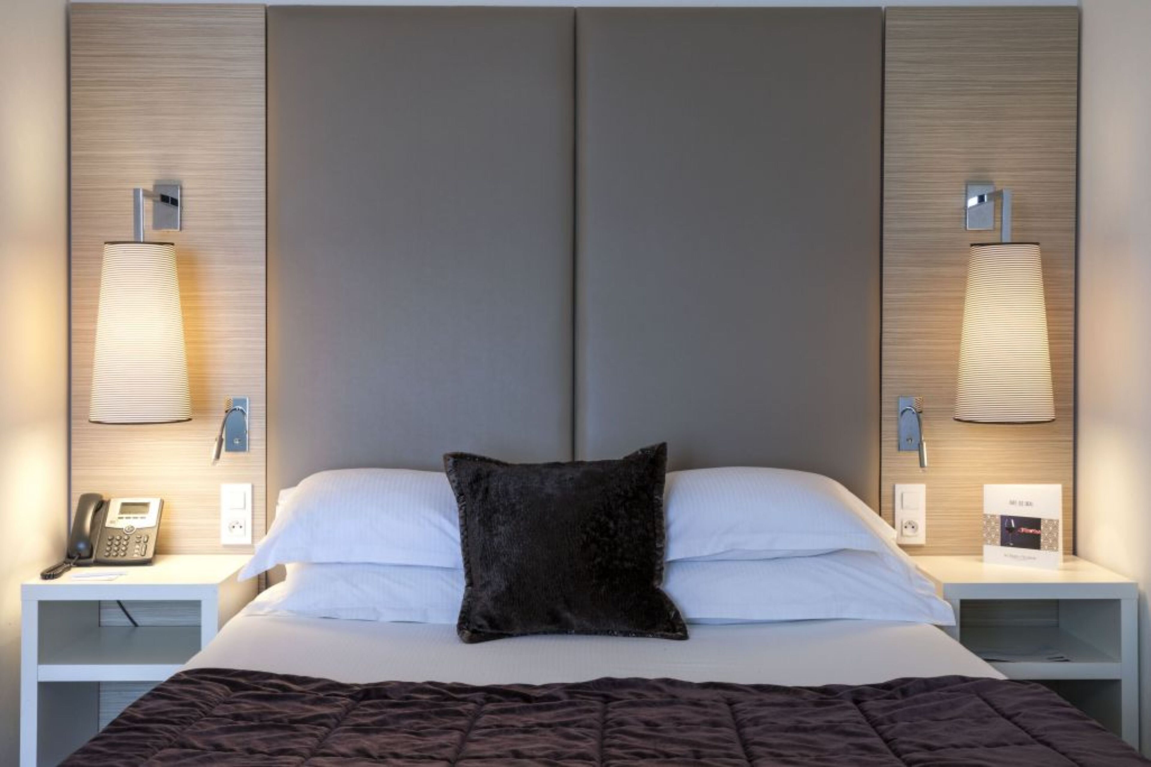 A hotel room with a large bed, two bedside tables, a telephone, and wall-mounted lamps.