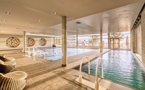 Une grande piscine intérieure à l’eau claire, entourée de chaises longues et dotée d’un sol carrelé.