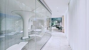 A modern interior with glass walls, white furniture, and a staircase leading to an upper level.