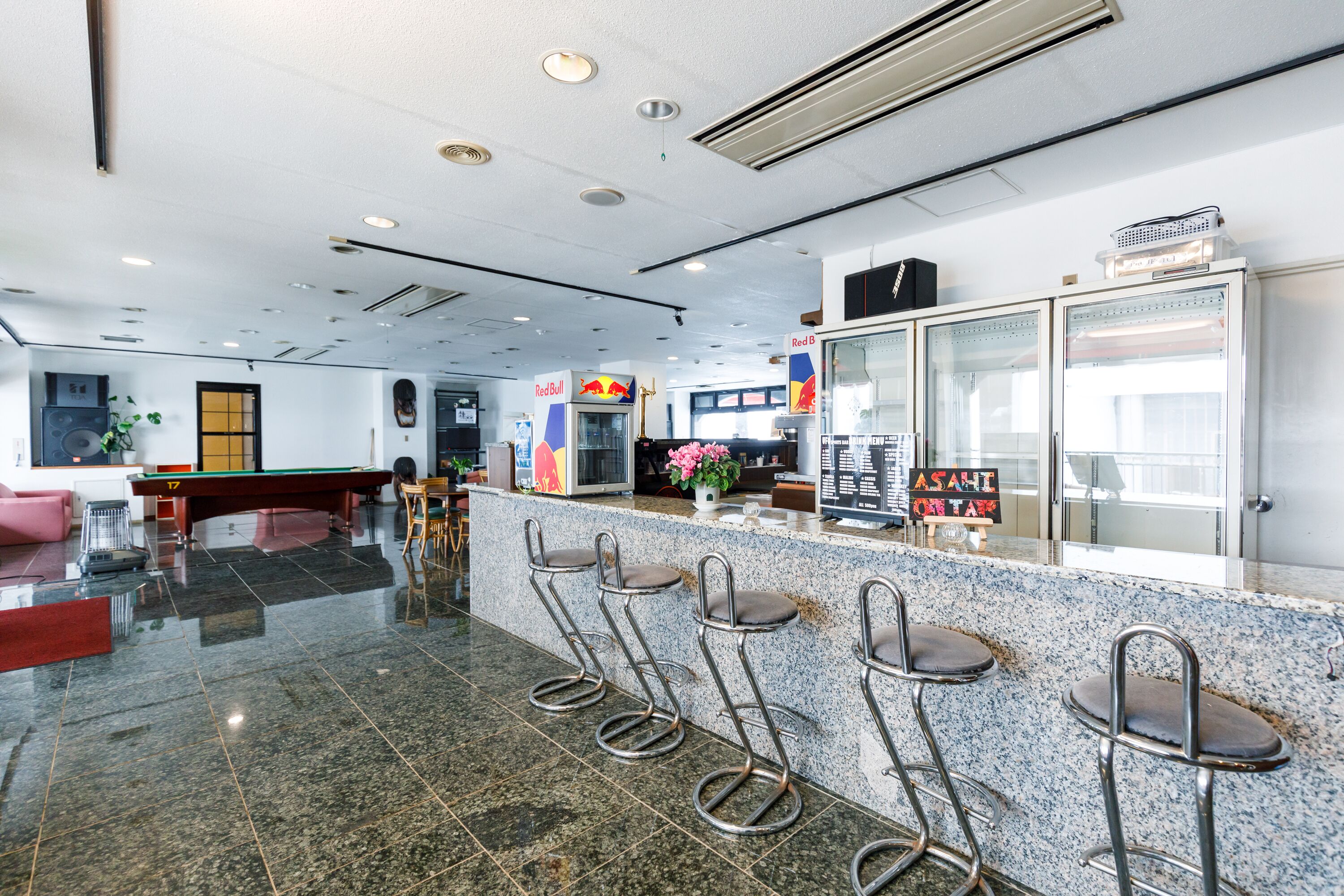 A bar area with a polished granite countertop, metal bar stools, and a Red Bull refrigerator.