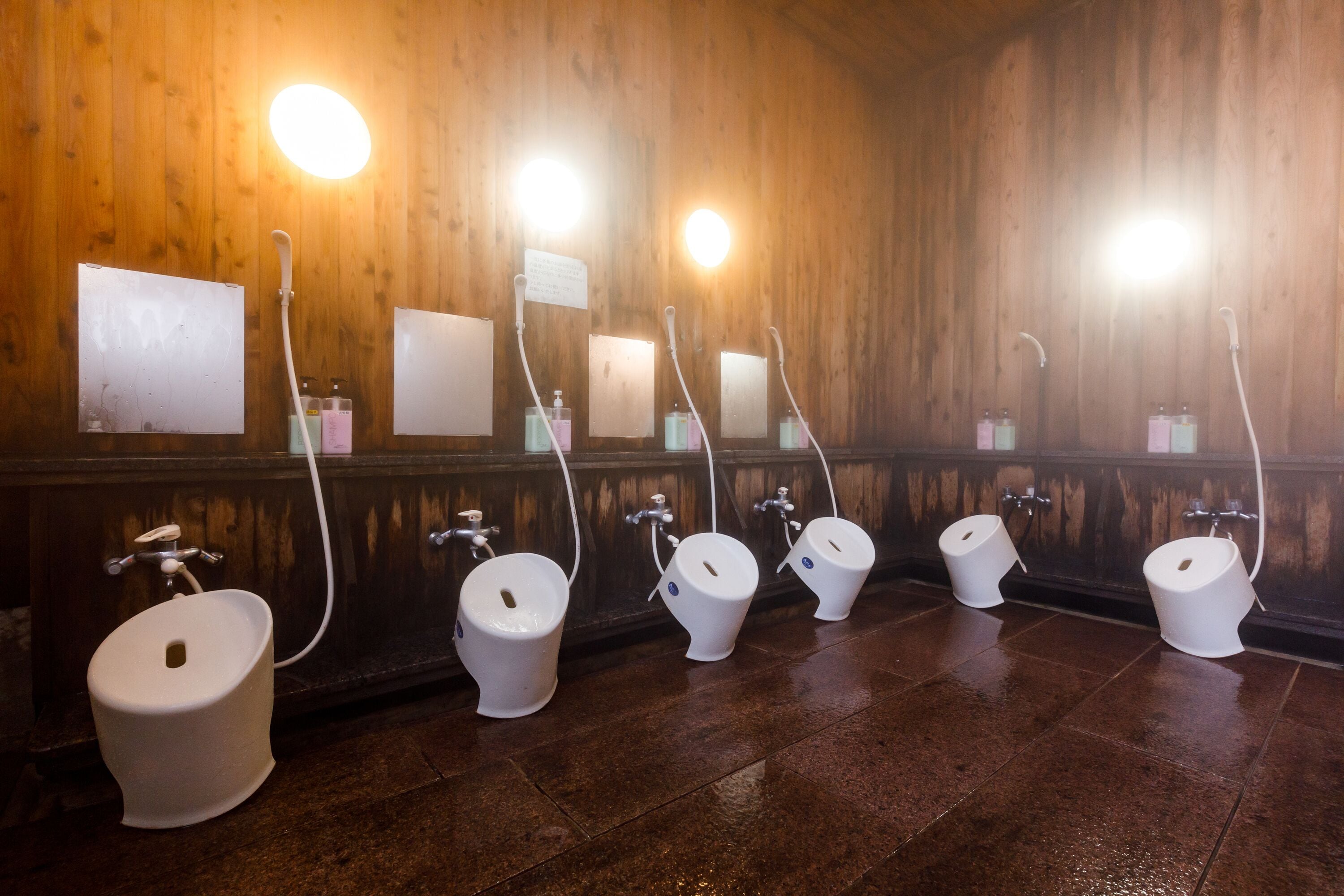 A public restroom with multiple urinals and sinks, wooden walls, and overhead lighting.