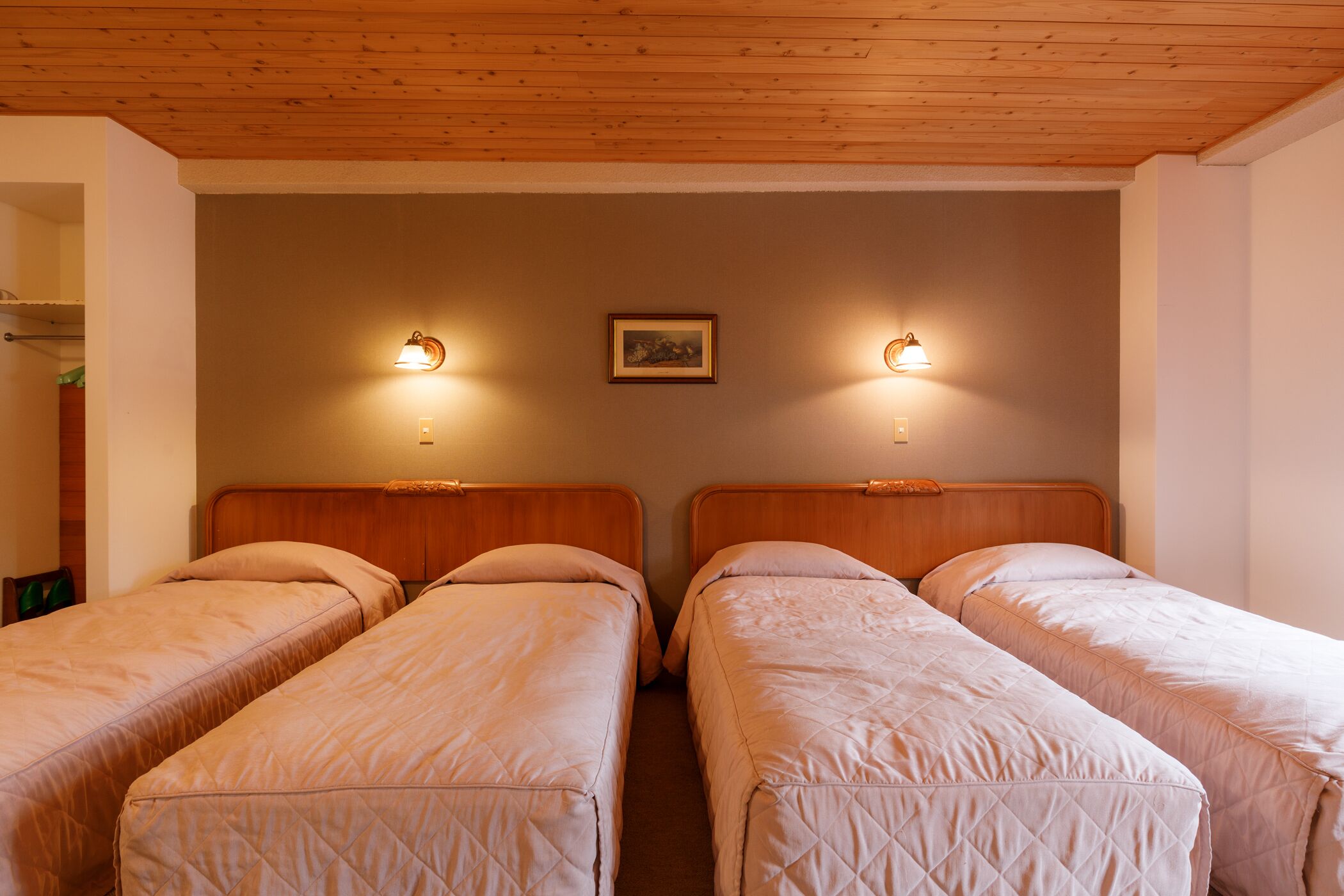 A room with two single beds, wooden headboards, and wall-mounted lights.