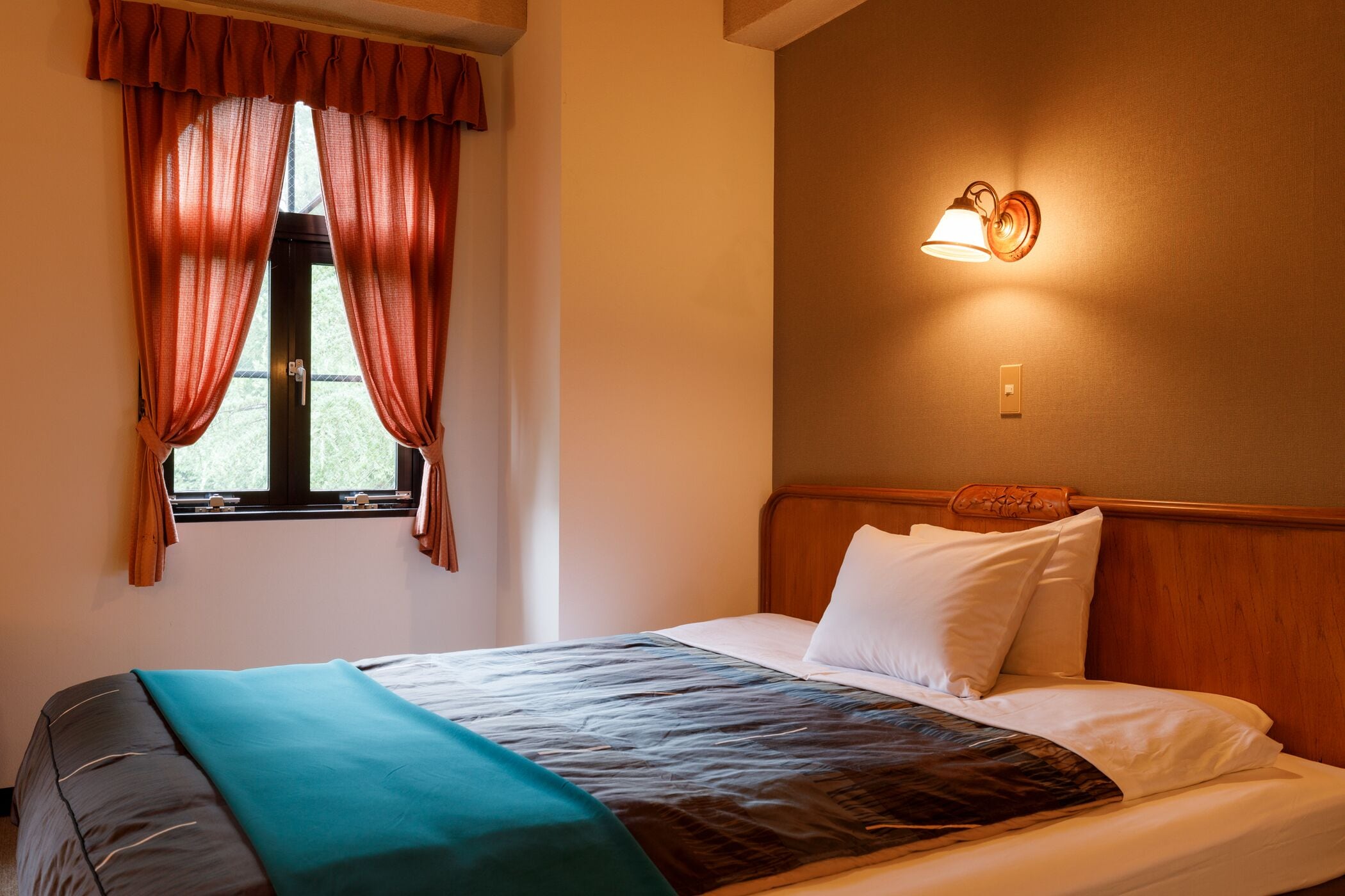 A hotel room with a bed, curtains, a wall-mounted light, and a window.