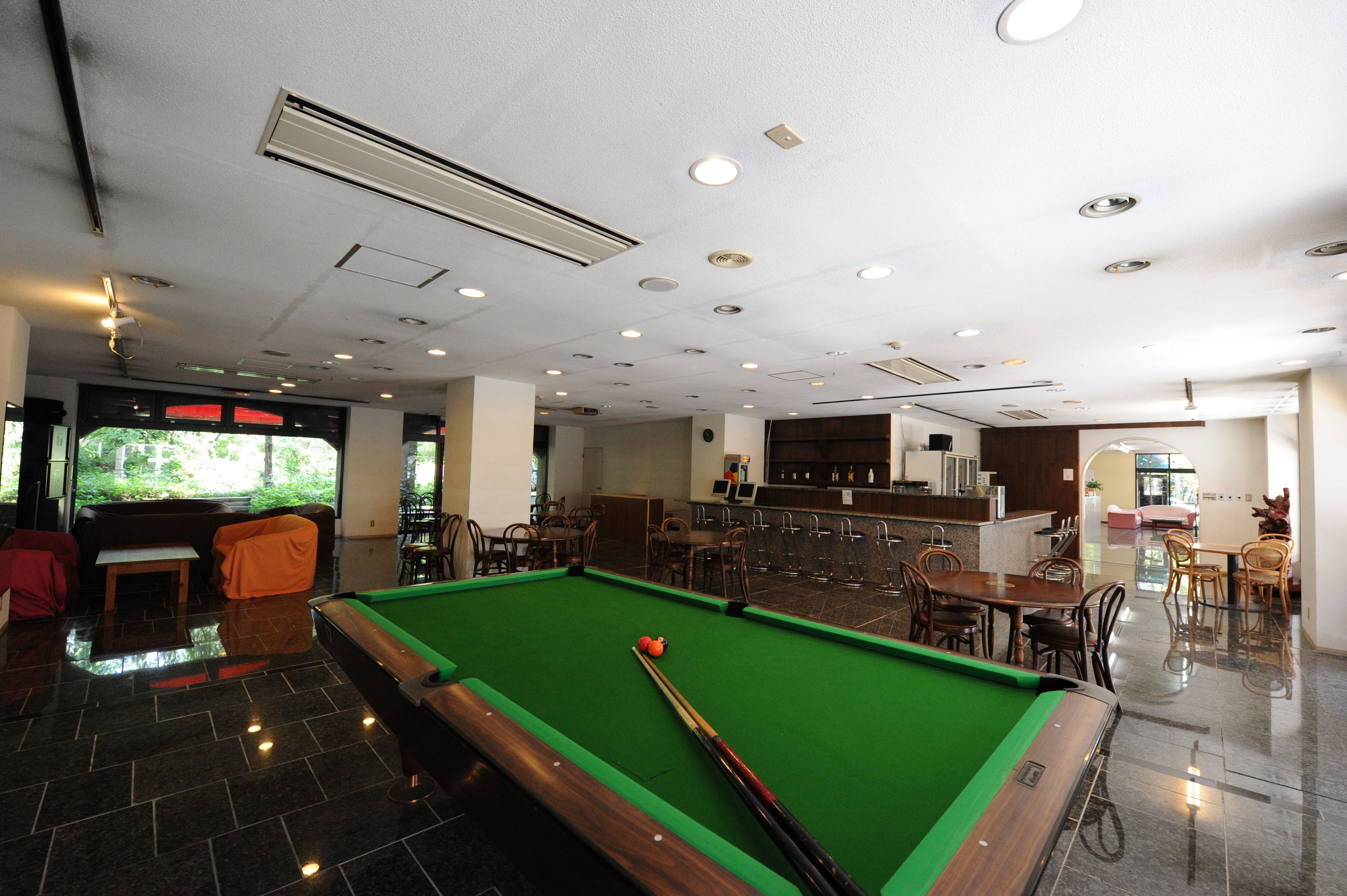A pool table in a well-lit room with a bar area and seating.