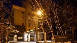 Un edificio con la entrada cubierta de nieve, una señal de parada de autobús y un banco de madera.