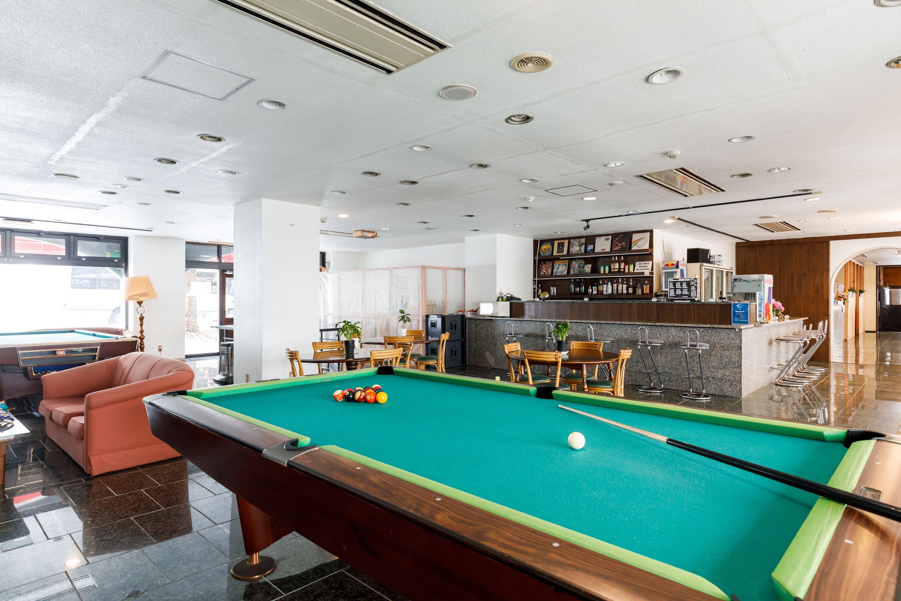 A pool table in a modern room with a bar area, seating, and a kitchen in the background.