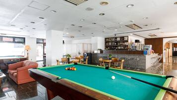 A pool table in a modern room with a bar area, seating, and a kitchen in the background.