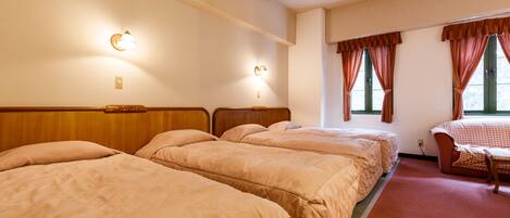 A hotel room with three beds, a wooden headboard, a small table, and two windows with curtains.