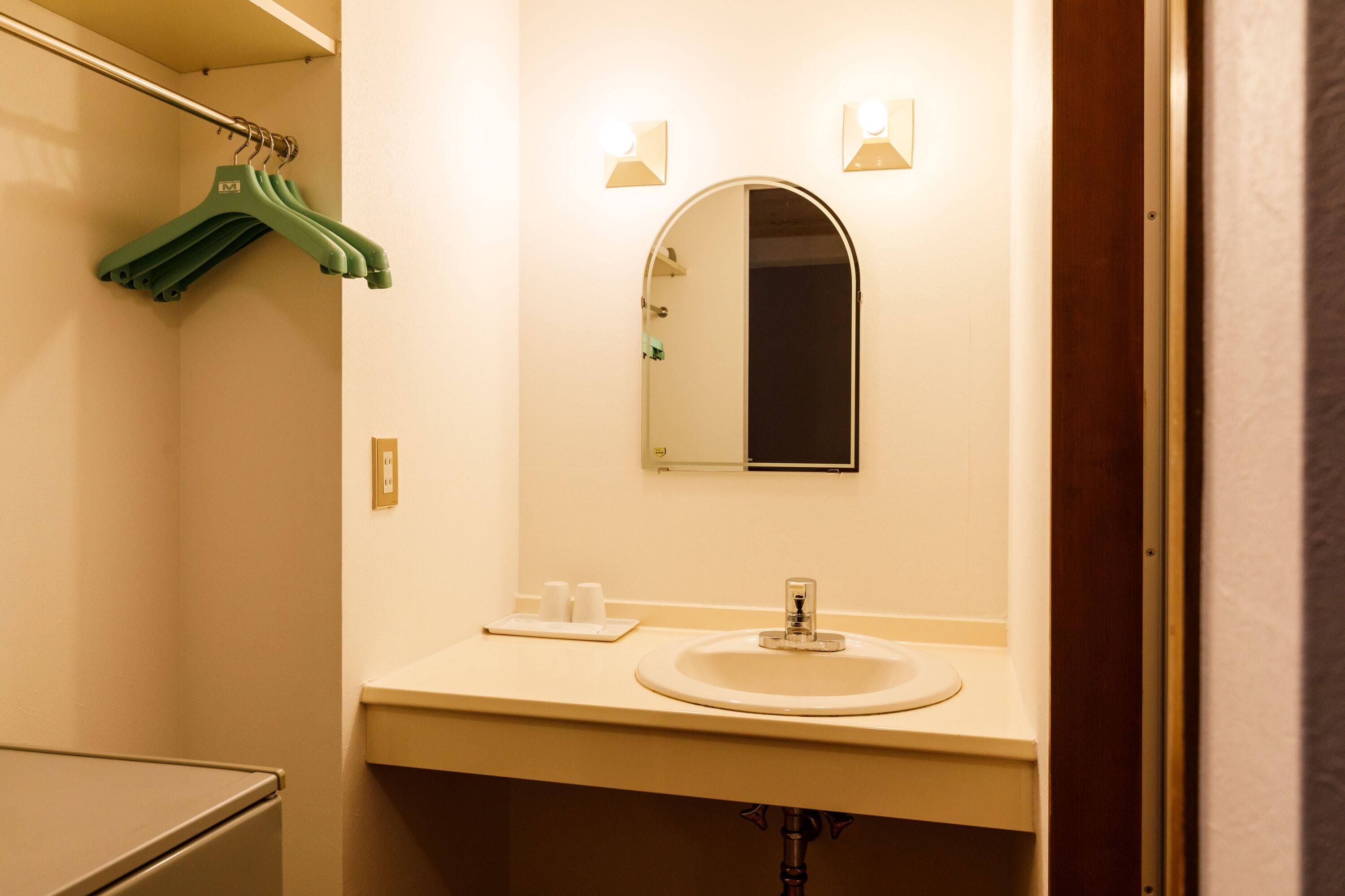 A bathroom with a sink, mirror, and green hangers on a rack.