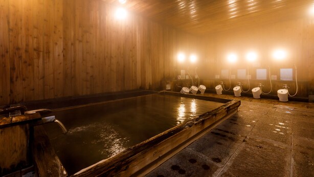 Una sauna de madera con una bañera grande de madera, múltiples luminarias y piso de baldosas.
