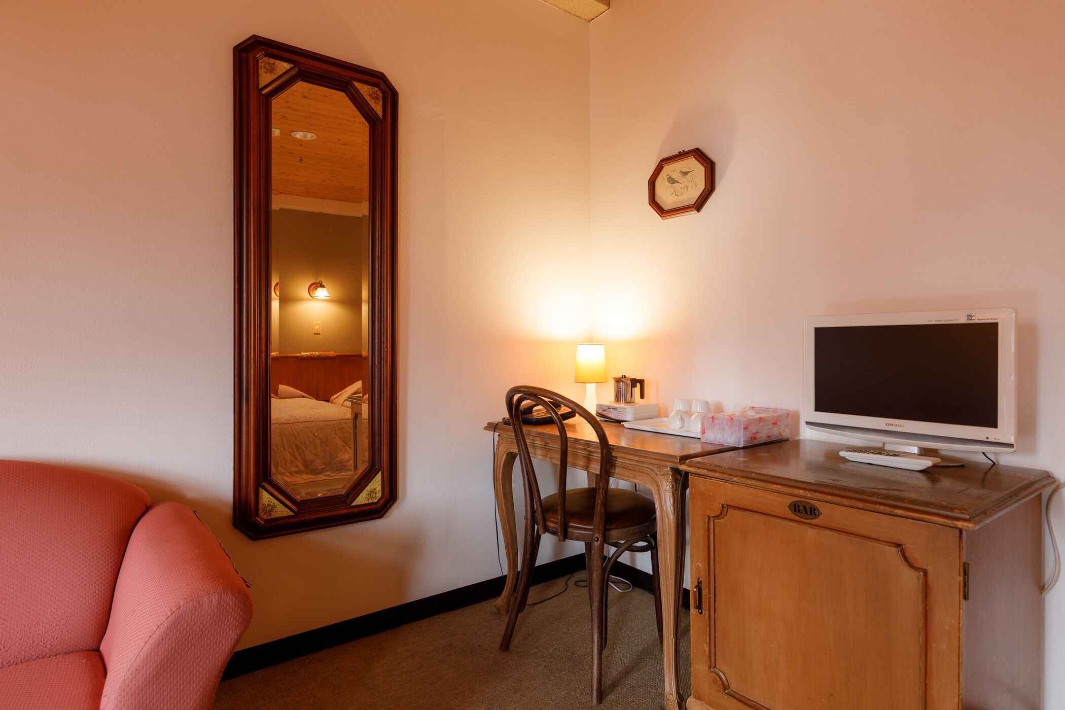A hotel room with a wooden desk, a chair, a television, a mirror, and a clock on the wall.