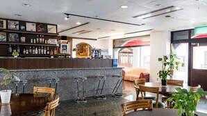 Una zona de bar con mostrador, taburetes y un área de estar con mesas y sillas.