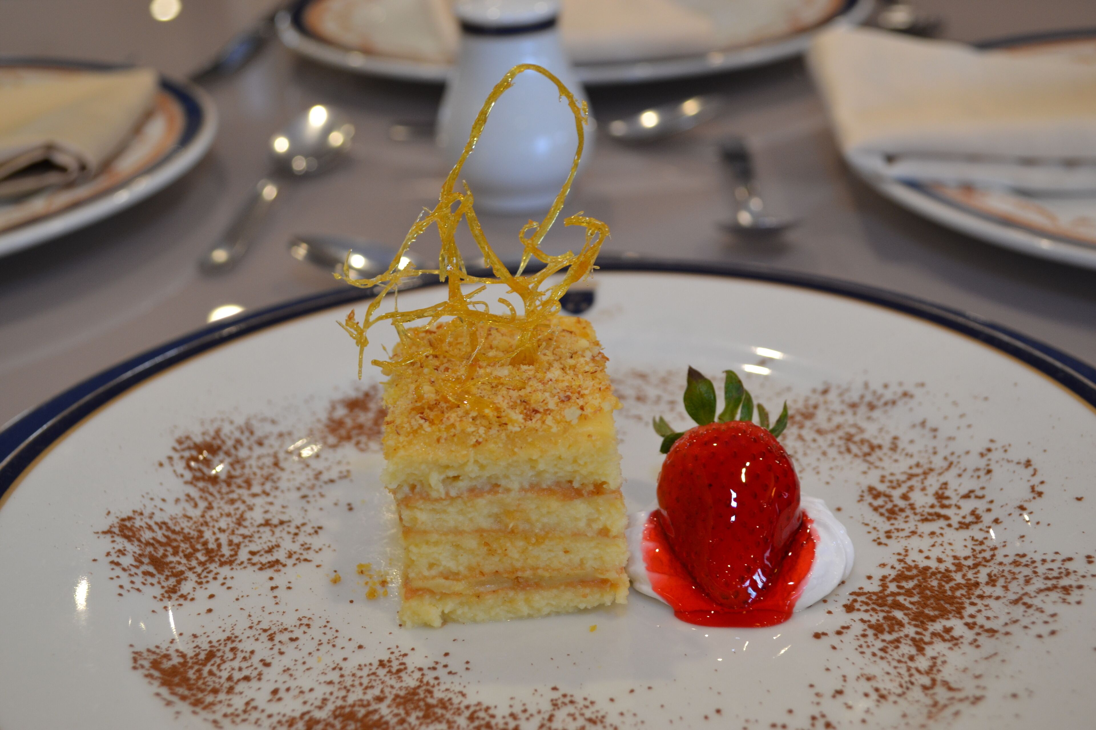 Un plat de postres amb un pastís en capes, una fragaria i sucre glas.