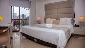Habitación de hotel moderna con una cama grande, dos lámparas de noche, un escritorio con silla y un balcón con vistas a la ciudad.