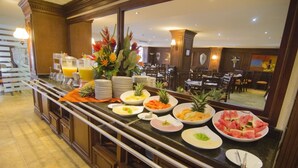 Montaje de bufé con diversas frutas y bebidas, un espejo que refleja el comedor y una escalera que sube a otro nivel.