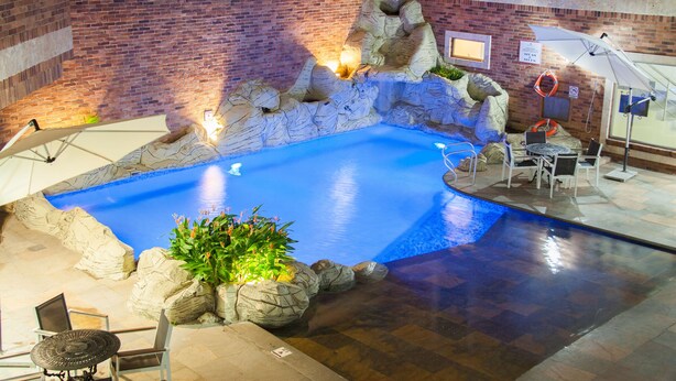 Una piscina interior con paisaje rocoso, zona de estar y una mesa con sillas.