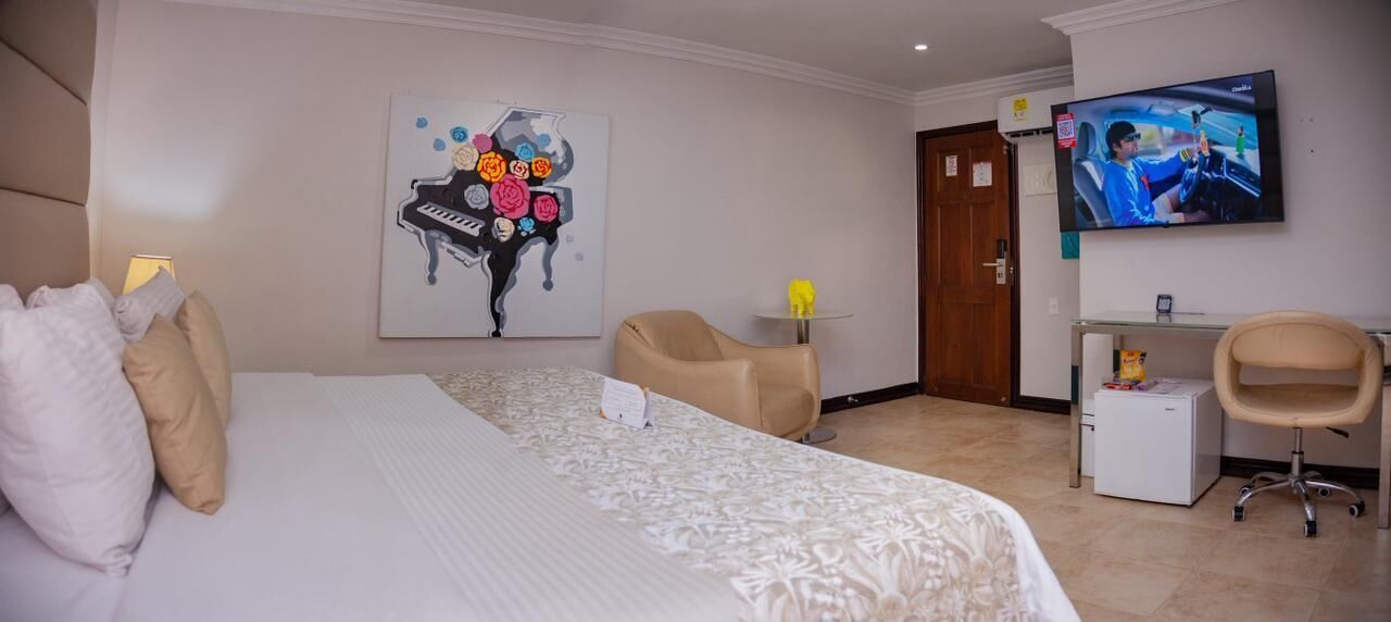 A hotel room with a large bed, a desk with a computer, a TV mounted on the wall, and a painting on the wall.