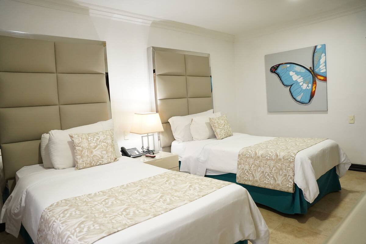 Two beds with headboards, a bedside table with a lamp, and a butterfly painting on the wall.