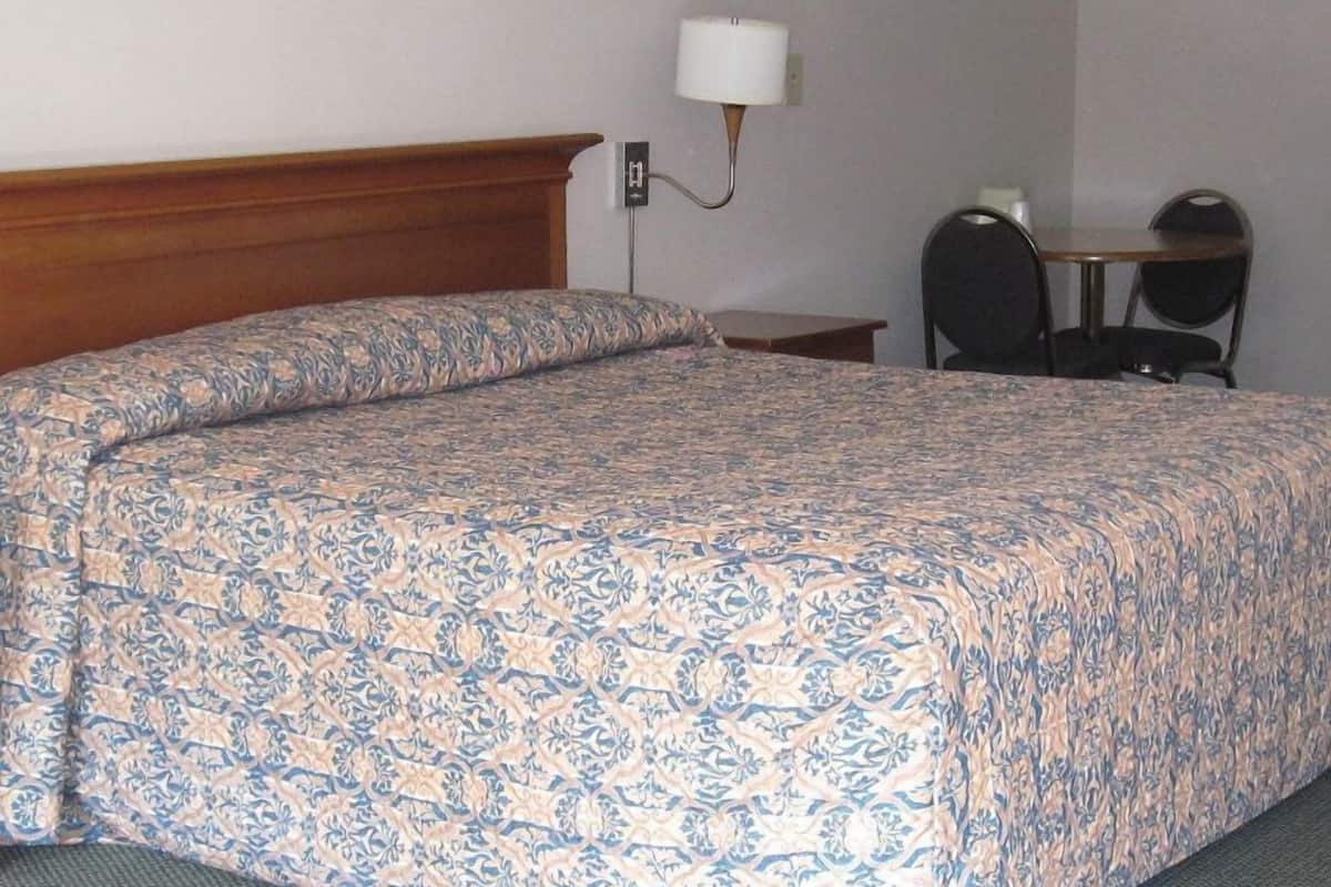 A hotel room with a large bed, a bedside table, a chair, and a lamp.