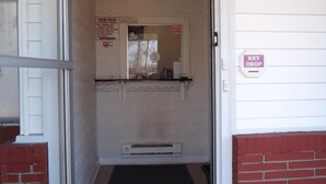 A hotel entrance with a glass door, a key drop, and a small air conditioning unit on the wall. - Budget Motor Inn - Mahopac (Mahopac)