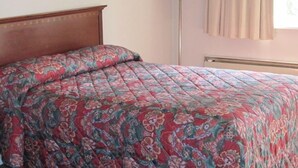 A bed with a floral-patterned bedspread, a bedside lamp, and a window with curtains. - Budget Motor Inn - Mahopac (Mahopac)