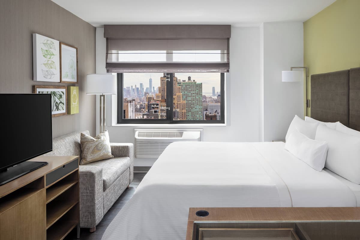 A hotel room with a large bed, a television, a sofa, and a city view.