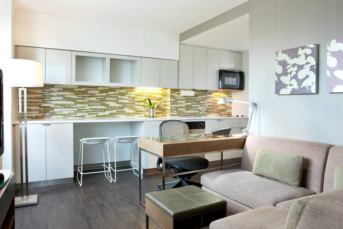 A compact living space with a kitchenette, a sofa, a TV, and a dining area with two bar stools.