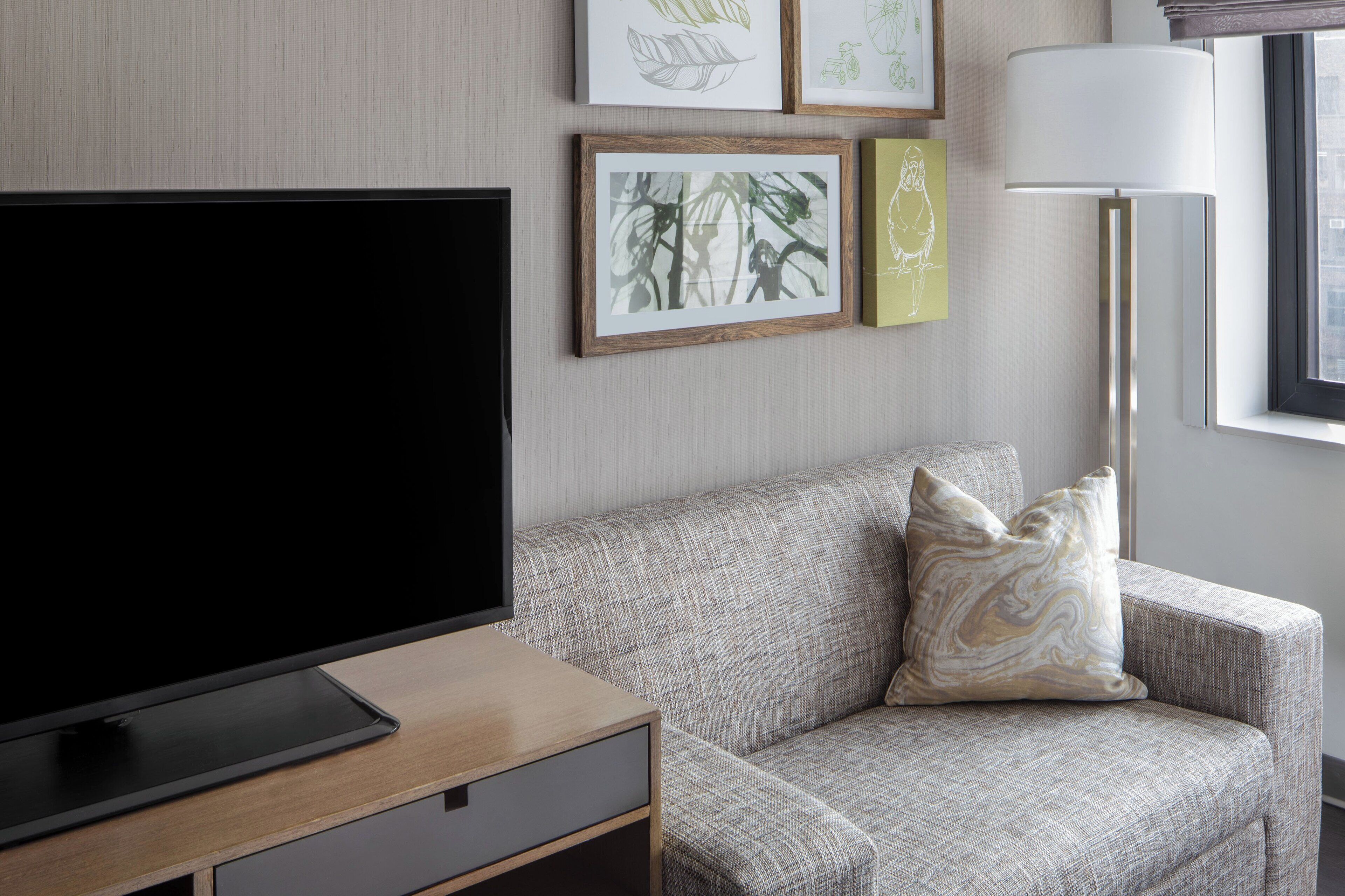 A modern living room with a flat-screen TV, a sofa with a patterned throw pillow, and framed artwork on the wall.