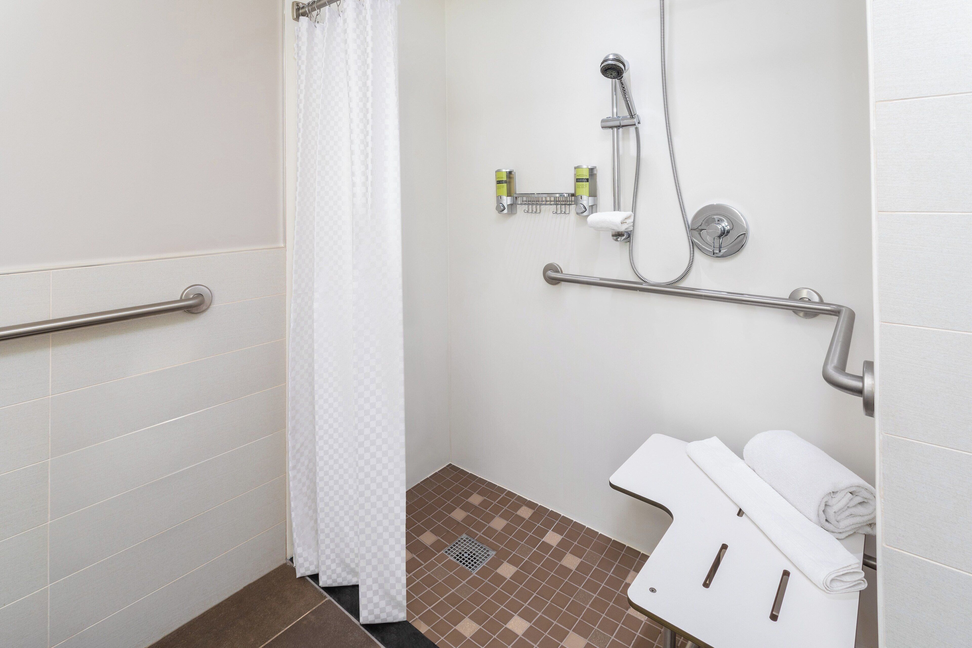 A bathroom with a shower, grab bars, a towel rack, and a toilet.