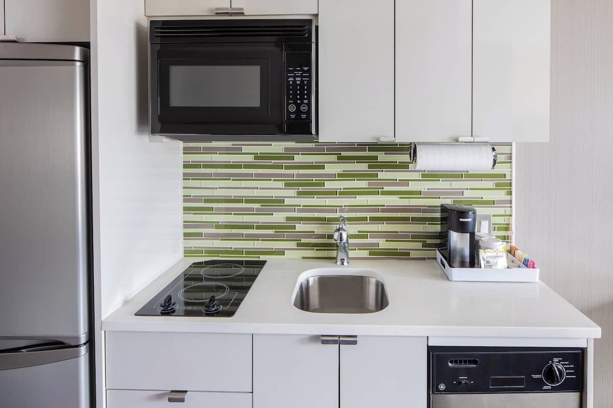A modern kitchen with a stainless steel refrigerator, a black microwave, a white countertop, a stainless steel sink, and a dishwasher.