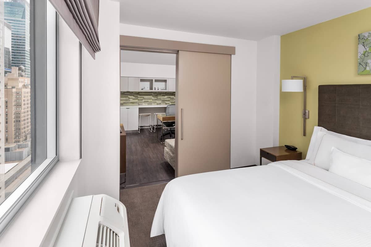 A hotel room with a bed, a desk, and a kitchenette.