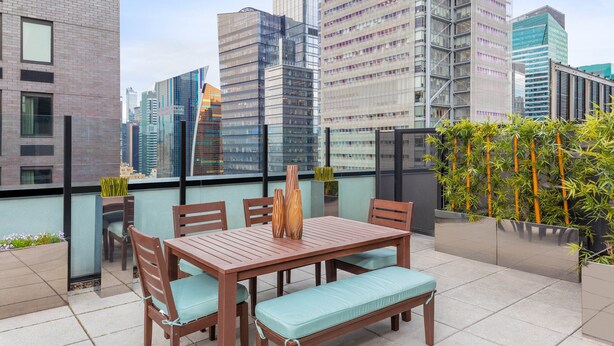 A rooftop terrace with a wooden table and chairs, surrounded by tall buildings.