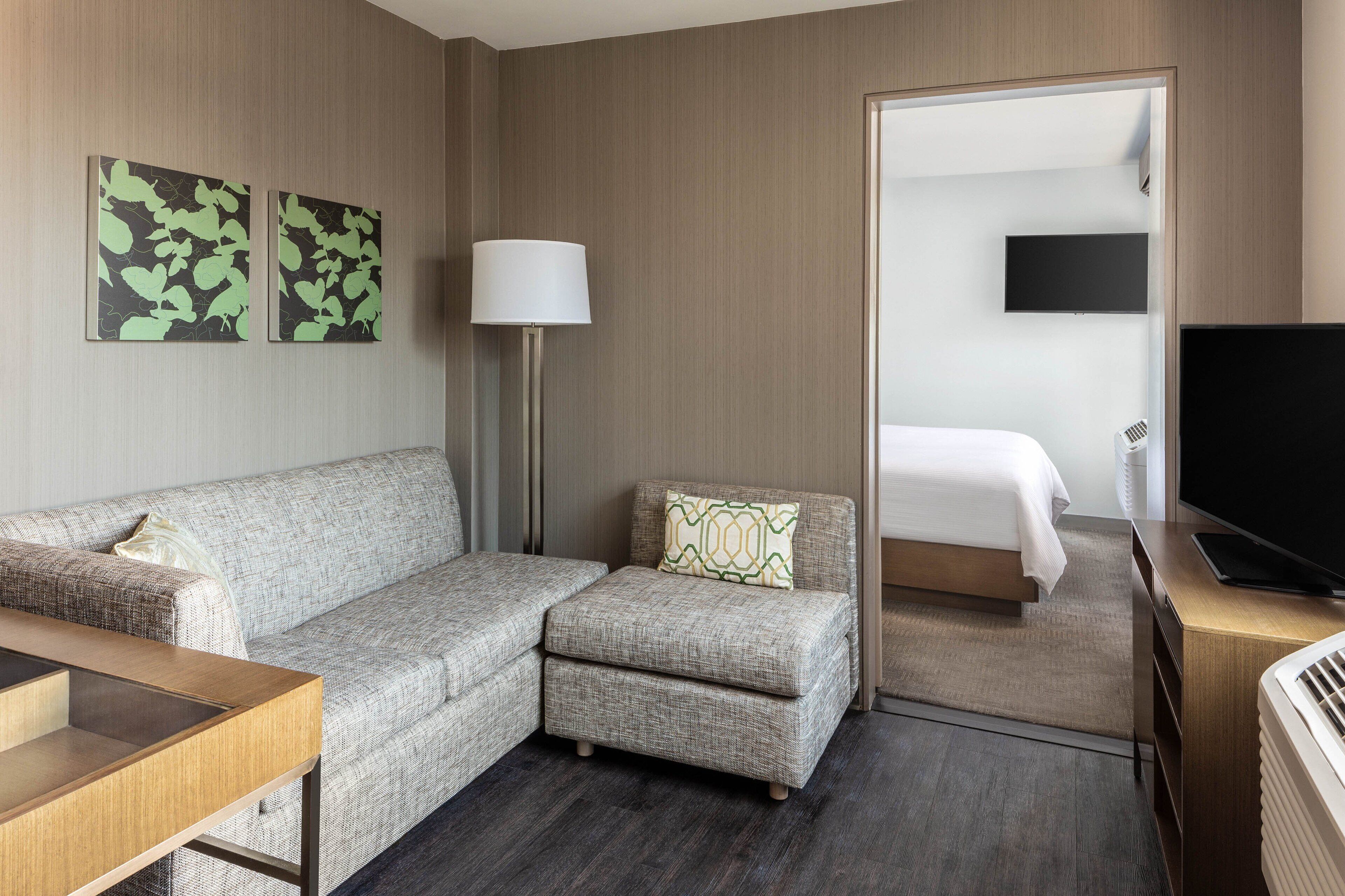 Ein Hotelzimmer mit einer Couch, einem kleinen Sessel, einer Lampe, einem Fernseher und einem Bett.