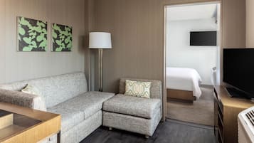 Ein Hotelzimmer mit einer Couch, einem kleinen Sessel, einer Lampe, einem Fernseher und einem Bett.