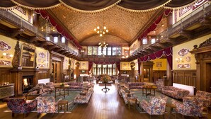 A grand hall with ornate woodwork, multiple seating areas, and a central chandelier.