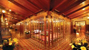 A hotel lobby with a central glass booth, wooden flooring, and potted plants.