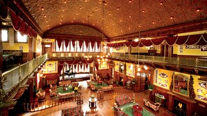 A grand, ornately decorated interior with a high ceiling, multiple levels, and a central seating area with floral upholstery.