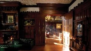 A grand room with a fireplace, leather sofa, and wooden paneling.