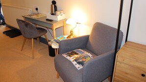 A room with a grey armchair, a desk with a lamp, a radiator, and a magazine on the armchair. - Woodlands Country House (Wigton)
