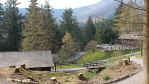 A rustic lodge with a wooden deck, surrounded by dense forest and mountains in the background. - Woodlands Country House (Wigton)