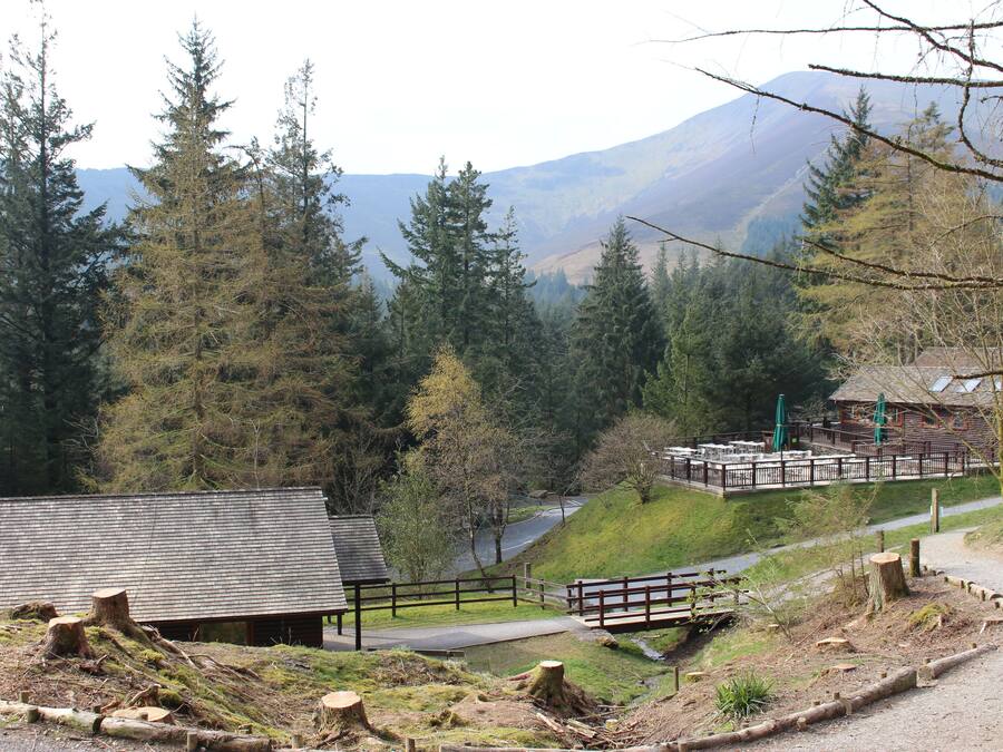 A rustic lodge with a wooden deck, surrounded by dense forest and mountains in the background.