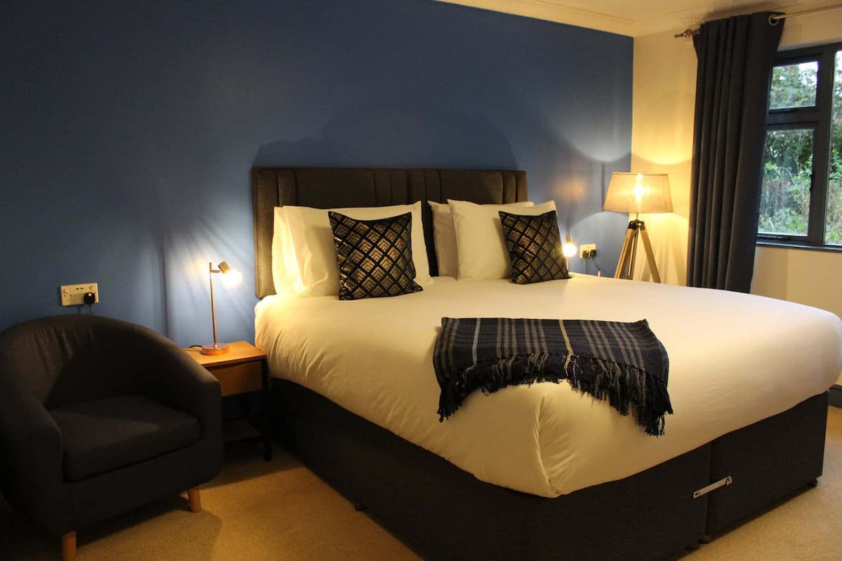 A neatly made bed with a dark headboard, a bedside lamp, and a chair.
