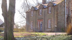 A stone building with a traditional design, featuring a central entrance with a door and windows on the upper floor. - Woodlands Country House (Wigton)