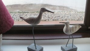 Two bird sculptures on window sills with a view of a rocky shoreline. - Yacht Bay View (Morecambe)