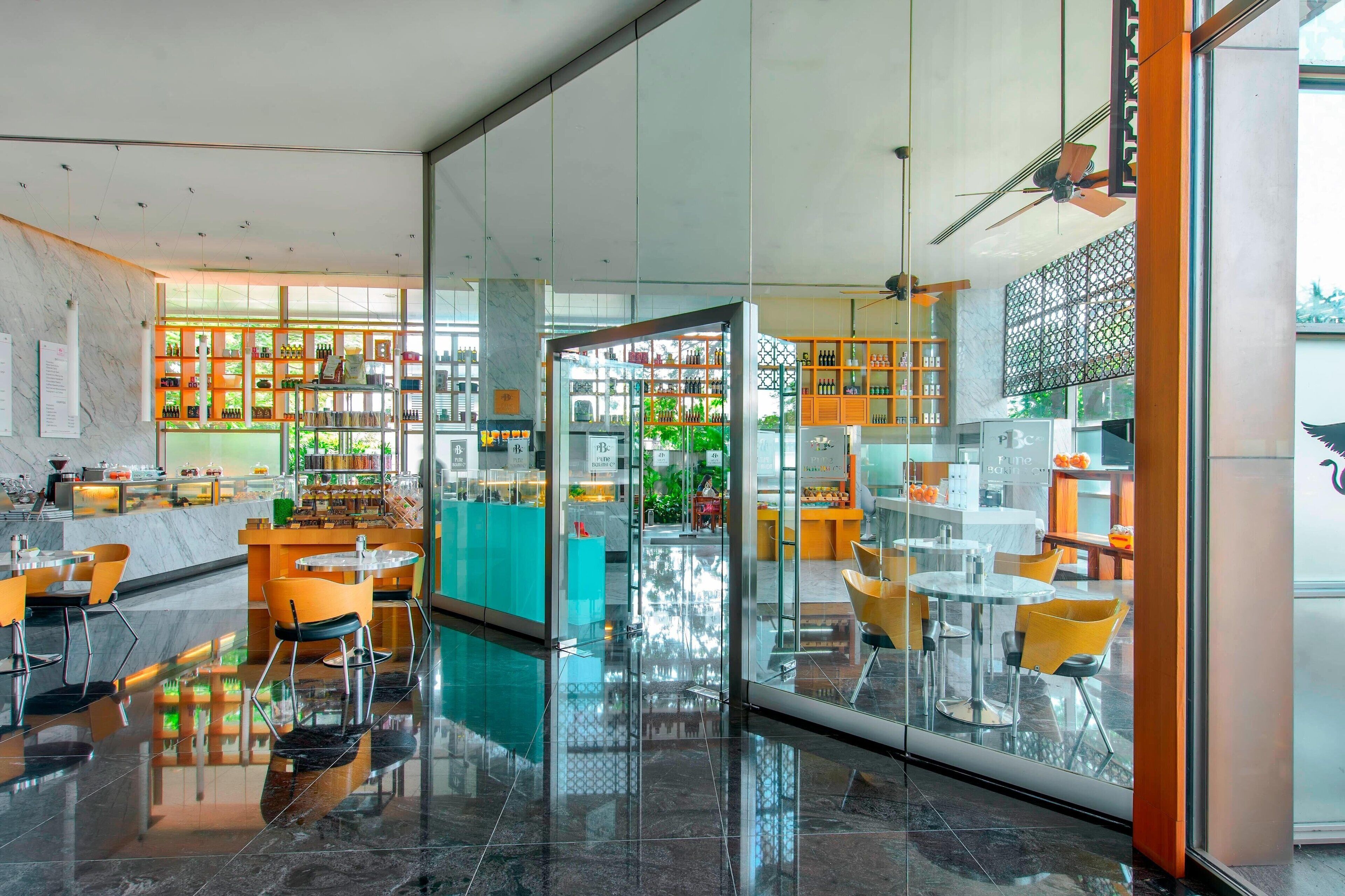 Un hall d’hôtel moderne doté d’une cloison en verre, d’espaces aménagés pour s’asseoir et de diverses commodités, notamment un bar et un comptoir de réception.