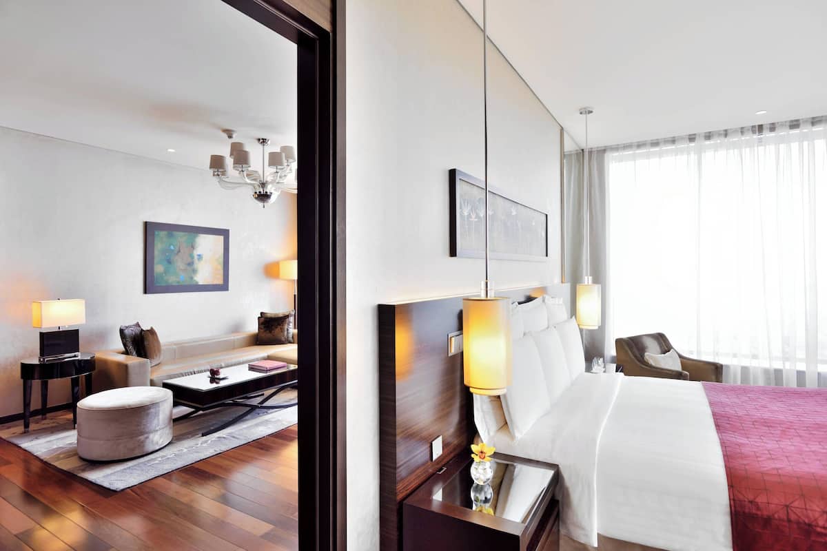 Habitación de hotel moderna con una cama grande, un sofá, un escritorio y una silla. Hay un cuadro en la pared y una ventana con cortinas.