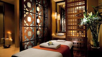 Experience tranquility in this serene spa room, featuring a massage table, decorative flower, and elegant partition.